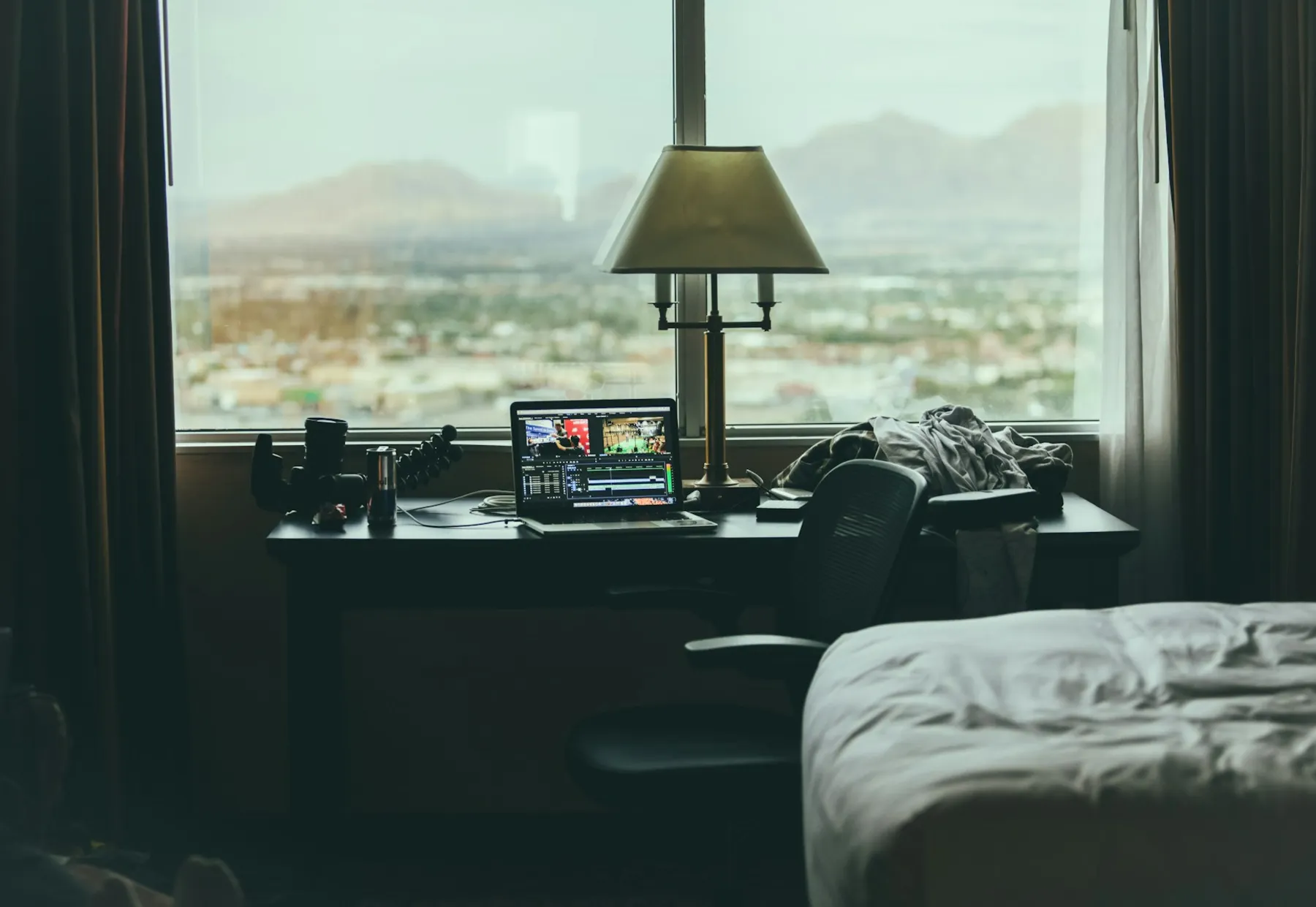 Laptop and desk lamp beside a large window overlooking a city